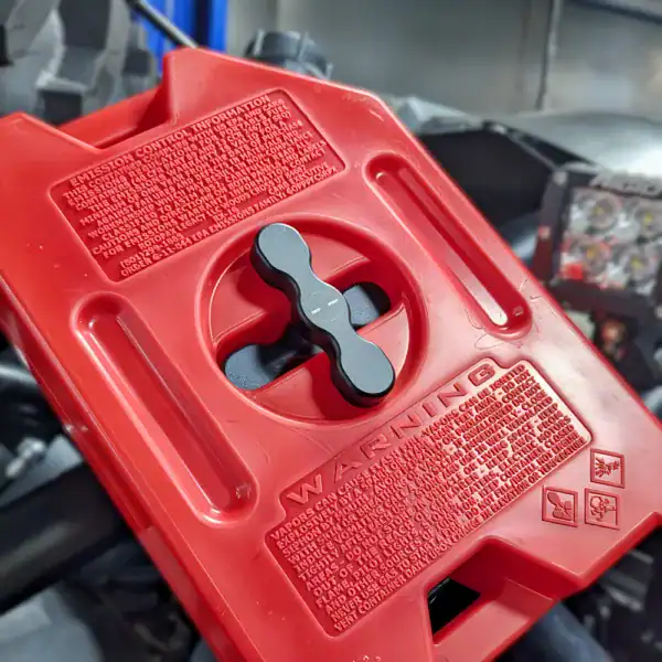 Close-up of red Rotopax gas can mounted on Polaris RZR with twist handle and warning label visible