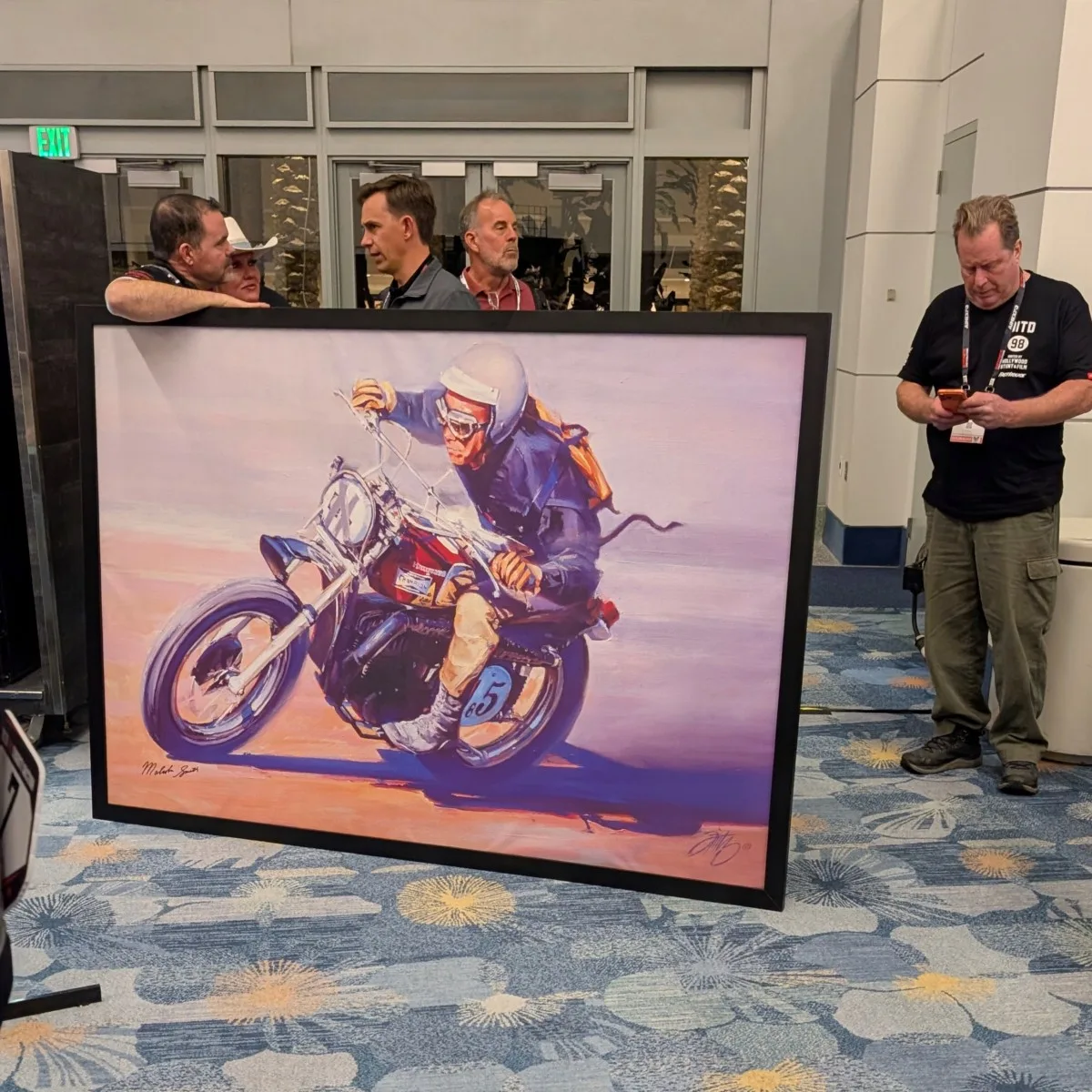 Alexander Smith holding iconic Malcolm Smith racing painting during AIMExpo 2026 auction